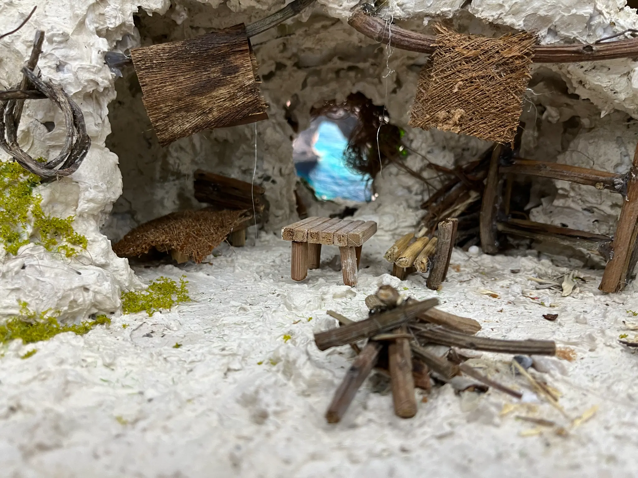 Inside the limestone cave shelter — wooden table, woven mat, distant turquoise pool